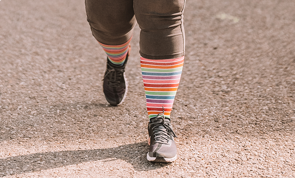 Beine von Person beim Joggen in schwarzen Laufschuhen und bunt gestreiften Sport Kompressionsstrümpfen für breite Waden